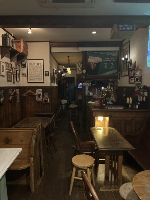 Ye Malthouse の店内。木のカウンターとテーブル、壁に並ぶ額縁。